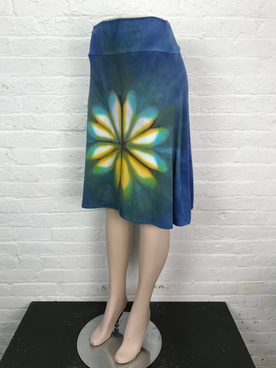 Hand-dyed bamboo/cotton jersey skirt with a fold-over waistband and flared shape, featuring a central petal burst in yellow, turquoise, and green on a blue-green background.