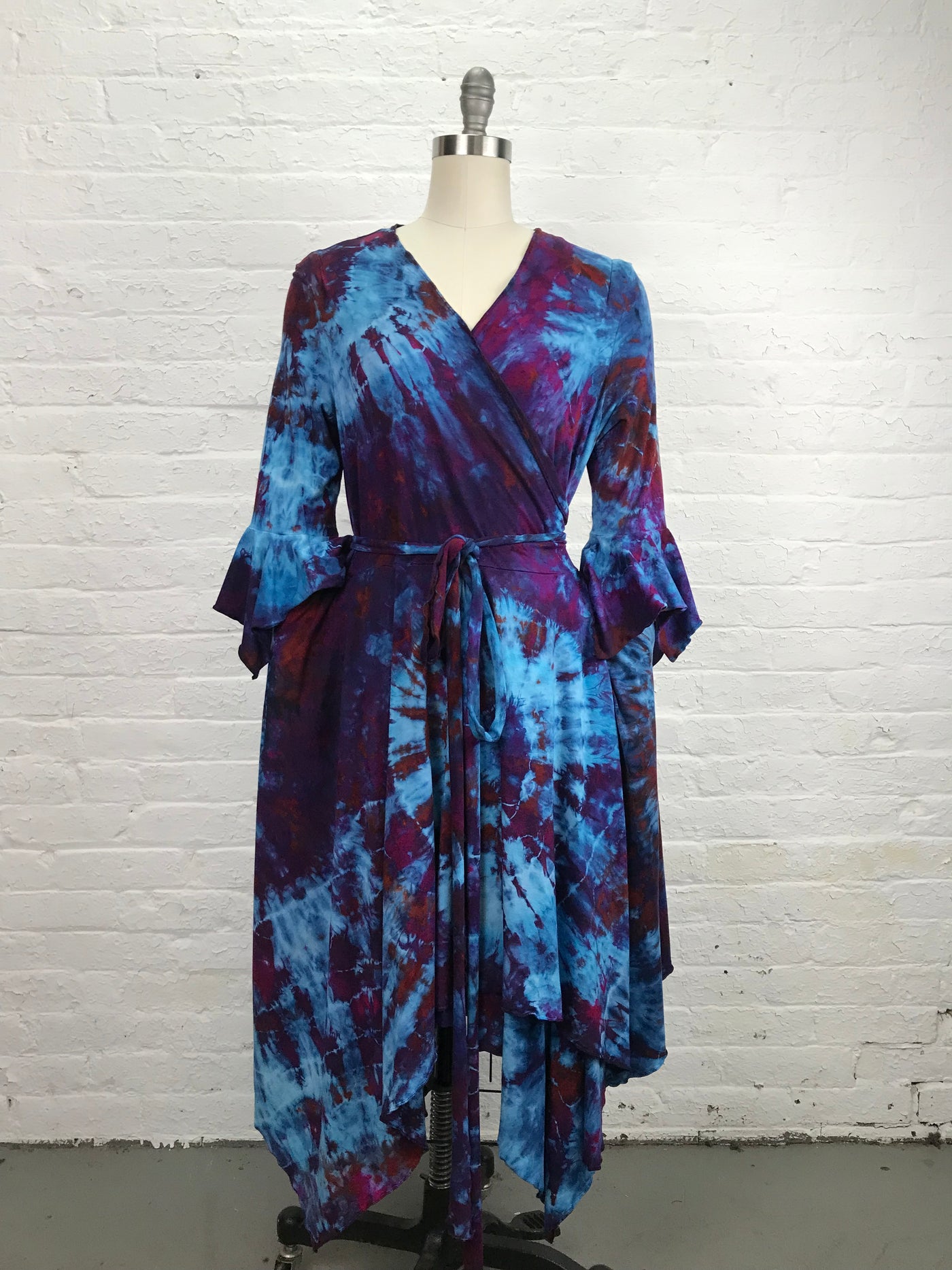 The Flamenco Wrap Dress in Falling Berries is a mix of blues and violets has an asymmetrical hemline and fitted elbow length sleeves that end in a delightful flounce. Wrap styling lends itself to an easy fit and a flattering V-neckline and pockets - front view