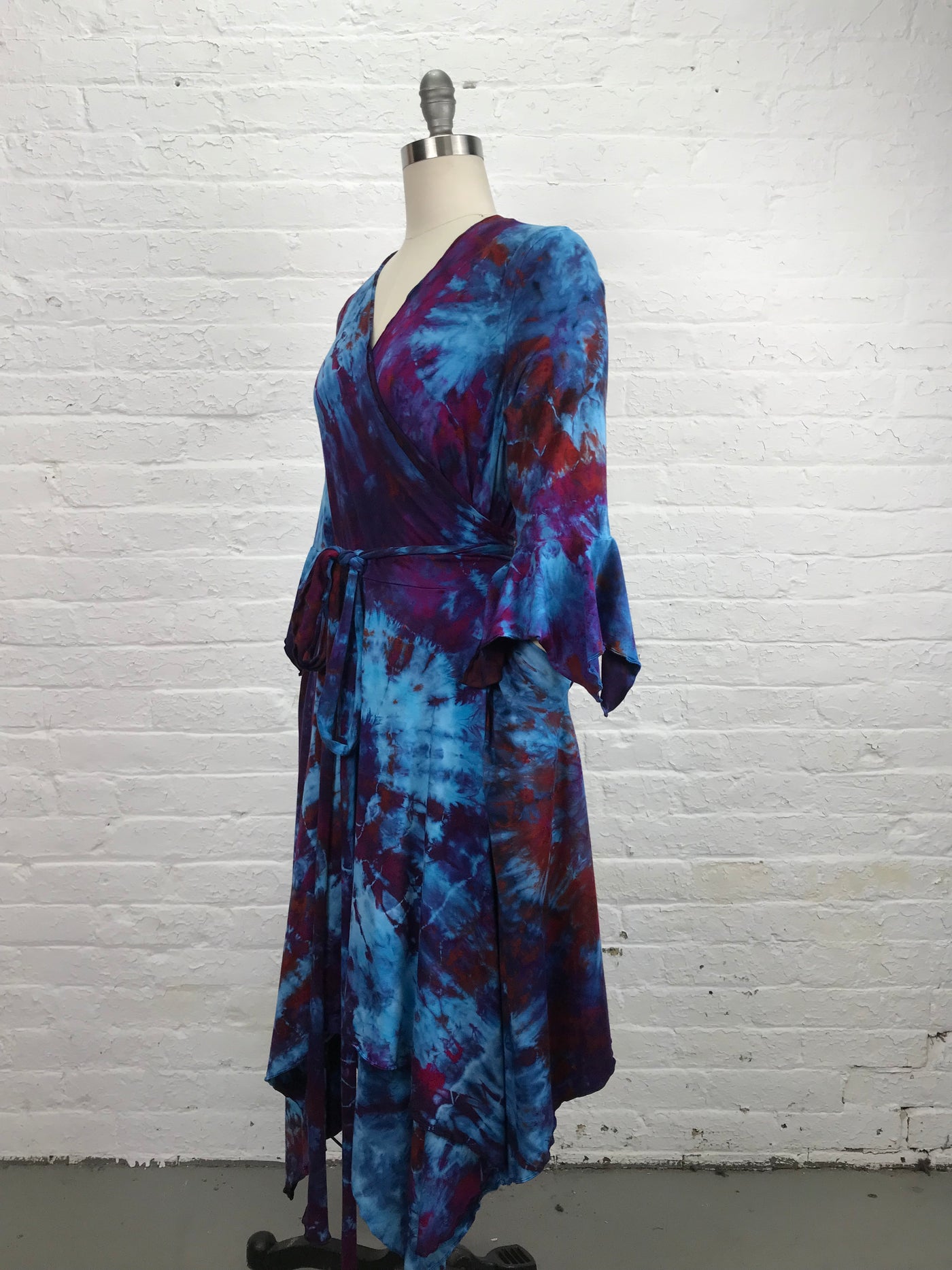 The Flamenco Wrap Dress in Falling Berries is a mix of blues and violets has an asymmetrical hemline and fitted elbow length sleeves that end in a delightful flounce. Wrap styling lends itself to an easy fit and a flattering V-neckline and pockets - side view